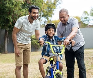 Picture of three generations of males teaching young boy to ride bike