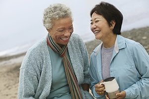 Two females enjoying a walk on the beach drinking coffee